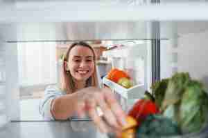 Happy woman taking vegetable from the fridge